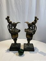Both brass table decorations with cherubs shown front and side views, overall condition and scale noted with green apple for size reference.