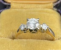 Ring displayed in original velvet presentation box, front view showing center and side diamonds.