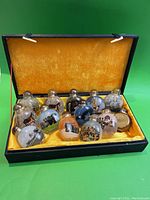 Front view of 11 snuff bottles displayed in a black box with bright yellow interior lining.