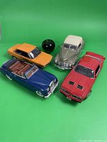Four intricately detailed metal model cars shown on green background alongside a green apple for scale.
