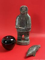 Hunter and seal sculptures displayed together with black glass apple for scale