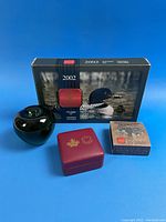 Three closed coin presentation boxes alongside a 3-inch apple for scale.