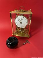 Front and side view of original Kundo German mantel clock with winding key and black glass apple for size reference.