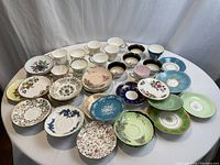 Full overview of all cups and saucers arranged on table, showing variety of patterns and colors.