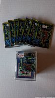 Seven unopened Deathmate card packs laid out on surface with one clear card display case containing cards topped with a $10 price sticker.