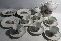 Photo showing full tea set including teapot, sugar bowl, six cups with saucers and six lunch plates displaying colorful gnome character artwork on white porcelain with gold trim