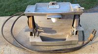Front view showing the bench grinder with two grinding wheels, base, and power cord.