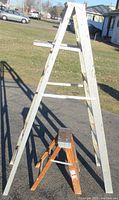 Photo showing the two folding ladders outside on a driveway with a grassy yard in the background. The taller aluminum ladder is 6 feet tall and the smaller wood ladder is 2 feet tall.