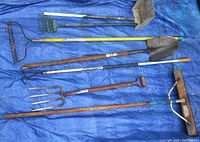 Full set of yard tools laid out on blue tarp showing broom, pitch fork, cultivator, shovel, rake, and scooper.