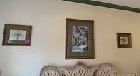 Wide shot of the three framed art pieces mounted on a wall above a couch, showing the large garden print in the center and two smaller palm tree prints on either side.