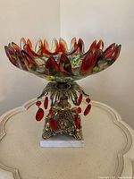 Full view of the art glass bowl on ornate metallic stand with marbled base, showcasing the colorful glass and red teardrop hanging crystals.