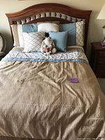 Full view of bed made with comforter and multiple pillows, featuring wooden headboard with spindle details.