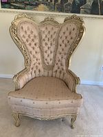 Full front view of a French provincial wingback chair showing tufted cream fabric upholstery with bee prints and ornate carved wood frame.