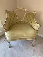 Front view of French Provincial chair showing tufted beige-green velvet upholstery, cane back rest and carved white distressed frame.
