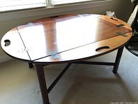 Full view of wooden Hickory Chair coffee table showing oval top with brass hinges and cut-out handles.