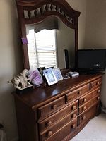 Full view of the wooden dresser with various items on top, including frames and a TV, showing the design and condition.