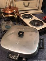 Photo showing all items in the lot including vintage electric double burner hot plate, large General Electric electric frying pan with lid, copper chafing pan on stand, and Corning Ware holders.