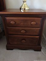 Front view of the wooden nightstand showing all three drawers and round knobs.