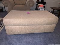 Top and front view of the rectangular ottoman showing tan textured fabric upholstery and cushioned top