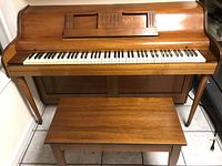 Front view of the Grand Piano Co. Metropolitan upright piano with matching bench in wooden finish, showing keyboard and music stand details.