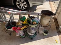 Wide view showing multiple ceramic pots stacked and arranged on metal plant stands, with various gardening supplies and hardware in packaging around them.