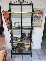Full view of black metal and glass shelf filled with various small items, showing swirl design and gold trim.