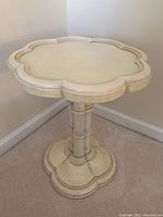 Front view of white wood accent table with scalloped round top and pedestal base showing speckled finish.