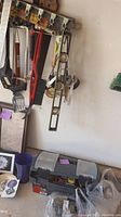 Craftsman plastic toolbox on the floor under a wall-mounted tool rack with hand tools and grilling utensils hanging, including spatulas and brushes.