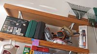 Overview showing boxed utility pump, power tools, socket set, lantern and sealant on wooden shelf