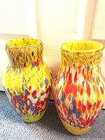 Front view of both heavy glass vases showing vibrant yellow base with multicolored spots in red, blue, white, and brown.