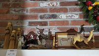 Wide shot showing entire lot of carved wooden camel, brass reindeer, plush girl doll, four angels including three straw angels, and framed angel artwork.