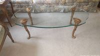 Side angle view showing the thickness of the glass top and ornate gold-tone carved wood legs.