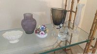 Shelf display of all six items: Lennox trinket dish (left), purple smoked vase (center left), Ainsley floral bone china (center), clear glass snail paperweight (center right), pressed glass bud vase (far right), smoked Orrefors vase (back right).