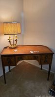 Full front view showing the wooden desk with leather top, lamp on corner, and visible scratches on the surface.