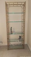 Front view of gold-colored metal etagere with four glass shelves against wall