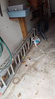 Full length view of the aluminum extension ladder lying on garage floor showing ladder rungs and side rails with some dirt and debris around.
