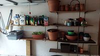 Shelves showing various garden chemicals, plastic watering cans, and multiple terracotta and plastic pots arranged on wooden shelves.