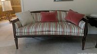 Front view of vintage wooden loveseat showing striped upholstery and pink and light gray pillows.