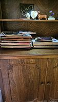 Wooden shelf holding stacks of vinyl LP albums and 45 rpm singles along with decorative figurines on top shelf.