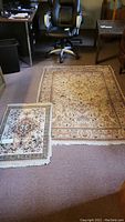 Overview of both area rugs side by side on carpeted floor under office chair showing patterns, sizes, and condition