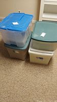 Five stacked assorted plastic storage tubs with various colored lids containing linens.