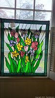 Full frontal view of stained glass panel hung in window showing floral design and chain.