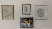 Four framed signed prints hanging on the wall including abstract and floral images