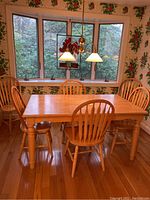 Full view of wood dining table with six matching chairs in a room with wooden floor and floral wallpaper.
