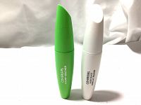 Two closed mascara tubes, one white (primer) and one green (mascara), standing upright on a white surface.
