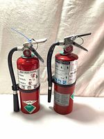 Two full view Amerex 5 lb ABC fire extinguishers showing labels, handles, and hoses.