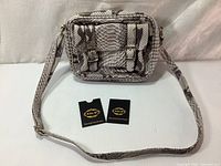 Full view of the rectangular snake print leather shoulder bag with two front buckle straps and adjustable shoulder strap. Two Ada. G brand tags visible in front of bag.