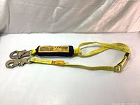 Yellow polyester lanyard with shock absorber and two double locking snap hooks laid flat on white surface.