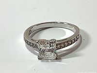 Front angle showing large square Swarovski crystal and embedded smaller crystals on white gold rhodium band.