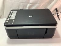 Front angled view of black HP Deskjet F4180 All-in-One Printer with visible power cable.